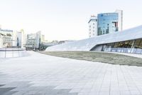 this is an empty and modern public plaza with modern architecture in the background, including a huge white building with windows