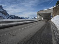 the snow covered mountains are in the distance as an empty mountain road passes under a bridge