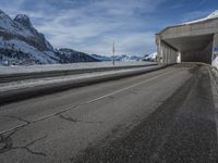 the snow covered mountains are in the distance as an empty mountain road passes under a bridge