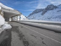 the snow covered mountains are in the distance as an empty mountain road passes under a bridge