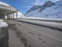 the snow covered mountains are in the distance as an empty mountain road passes under a bridge