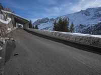 the snow covered mountains are in the distance as an empty mountain road passes under a bridge