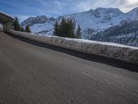 the snow covered mountains are in the distance as an empty mountain road passes under a bridge