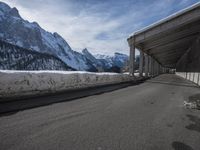 the snow covered mountains are in the distance as an empty mountain road passes under a bridge