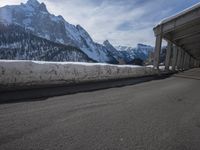 the snow covered mountains are in the distance as an empty mountain road passes under a bridge