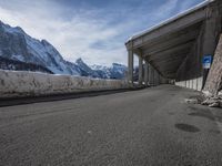 the snow covered mountains are in the distance as an empty mountain road passes under a bridge