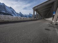 the snow covered mountains are in the distance as an empty mountain road passes under a bridge