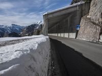 the snow covered mountains are in the distance as an empty mountain road passes under a bridge