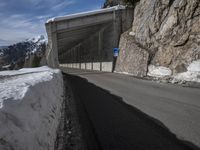 the snow covered mountains are in the distance as an empty mountain road passes under a bridge