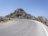 an empty mountain road next to the ocean with two red and white motorcycles parked on side