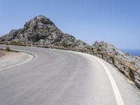 an empty mountain road next to the ocean with two red and white motorcycles parked on side