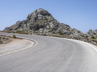 an empty mountain road next to the ocean with two red and white motorcycles parked on side