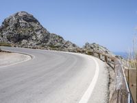 an empty mountain road next to the ocean with two red and white motorcycles parked on side