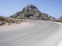 an empty mountain road next to the ocean with two red and white motorcycles parked on side