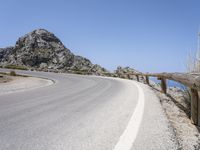 an empty mountain road next to the ocean with two red and white motorcycles parked on side