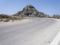 an empty mountain road next to the ocean with two red and white motorcycles parked on side