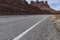 an empty mountain road passing through some cliffs near a dirt and grass covered hill top