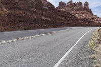 an empty mountain road passing through some cliffs near a dirt and grass covered hill top