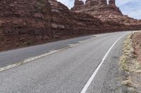 an empty mountain road passing through some cliffs near a dirt and grass covered hill top