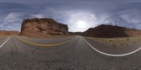 an upside down view of an empty mountain road with mountains in the background, from a fish - eye view mirror