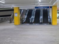 several empty moving stairs in the middle of an underground parking garage, with yellow columns