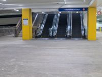 several empty moving stairs in the middle of an underground parking garage, with yellow columns