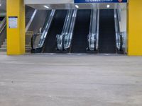 several empty moving stairs in the middle of an underground parking garage, with yellow columns