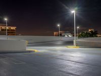 a empty parking lot lit up at night with buildings in the background and lights above