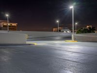 a empty parking lot lit up at night with buildings in the background and lights above