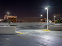 a empty parking lot lit up at night with buildings in the background and lights above