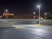 a empty parking lot lit up at night with buildings in the background and lights above