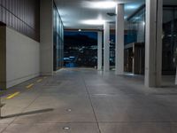 a walkway in an empty building with city skyline at night and clouds, behind it