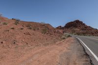 an empty open road surrounded by red rocks and a valley below it in the middle of the day