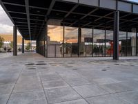 an empty outdoor walkway in front of a large building with many glass walls and metal columns