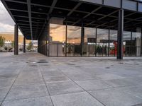 an empty outdoor walkway in front of a large building with many glass walls and metal columns