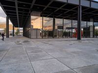 an empty outdoor walkway in front of a large building with many glass walls and metal columns