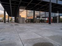 an empty outdoor walkway in front of a large building with many glass walls and metal columns