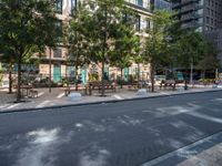 this is a view of an empty park area in a city setting where tables are on them, and one bench has a lamp