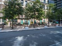 this is a view of an empty park area in a city setting where tables are on them, and one bench has a lamp