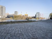 there is an empty park on the brick path next to water and buildings in the background