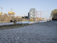 there is an empty park on the brick path next to water and buildings in the background