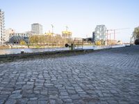 there is an empty park on the brick path next to water and buildings in the background