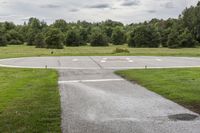 an empty park with a paved runway next to trees and a road lined with traffic markers