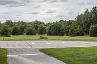 an empty park with a paved runway next to trees and a road lined with traffic markers