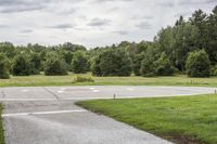 an empty park with a paved runway next to trees and a road lined with traffic markers