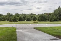 an empty park with a paved runway next to trees and a road lined with traffic markers