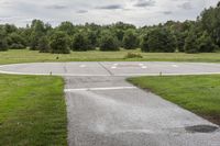 an empty park with a paved runway next to trees and a road lined with traffic markers