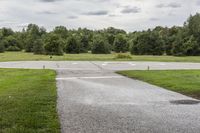 an empty park with a paved runway next to trees and a road lined with traffic markers