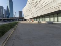 an empty parking area in front of a tall building with a blue sky behind it