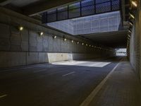 an empty parking area has lights illuminating it's side as a tunnel runs beneath the building